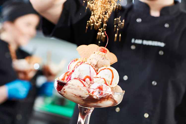 Nuts being sprinkled on an ice cream sundae